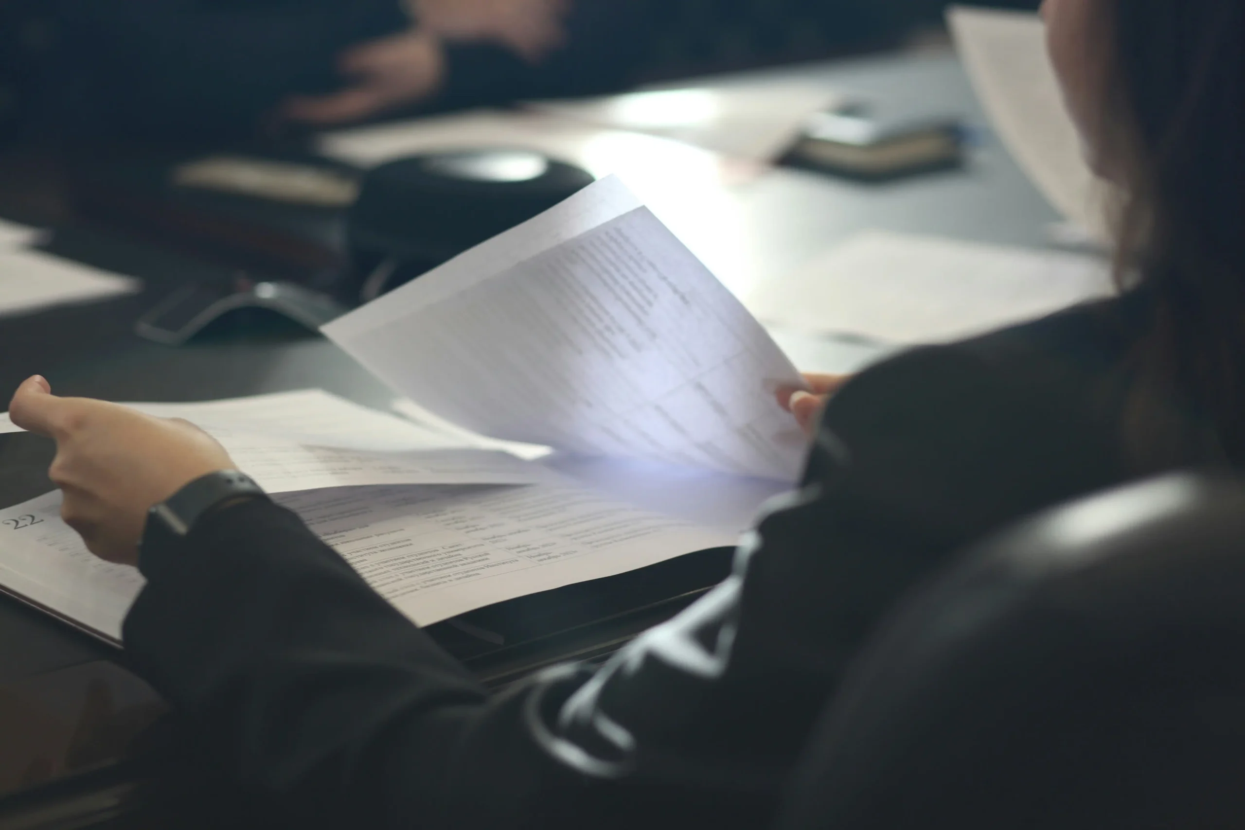 rofessionnel en train de consulter et trier des documents imprimés lors d'une réunion de travail, illustrant la gestion documentaire au sein d'une cellule de veille